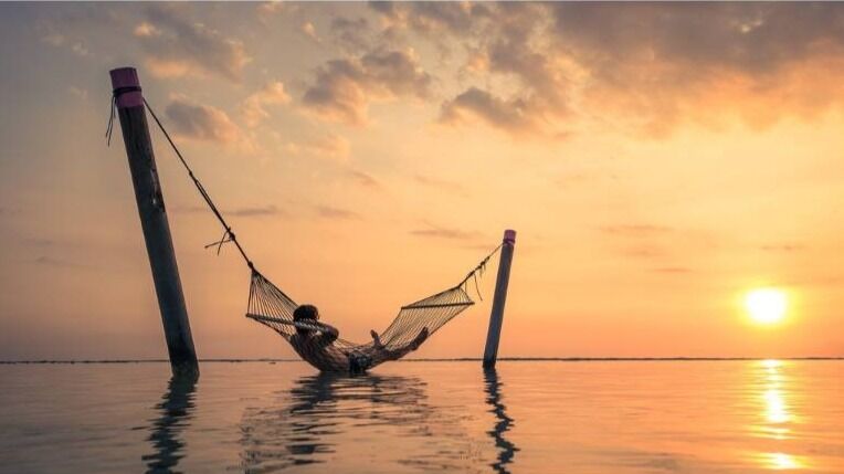man hanging in hammock over water between posts and without trees